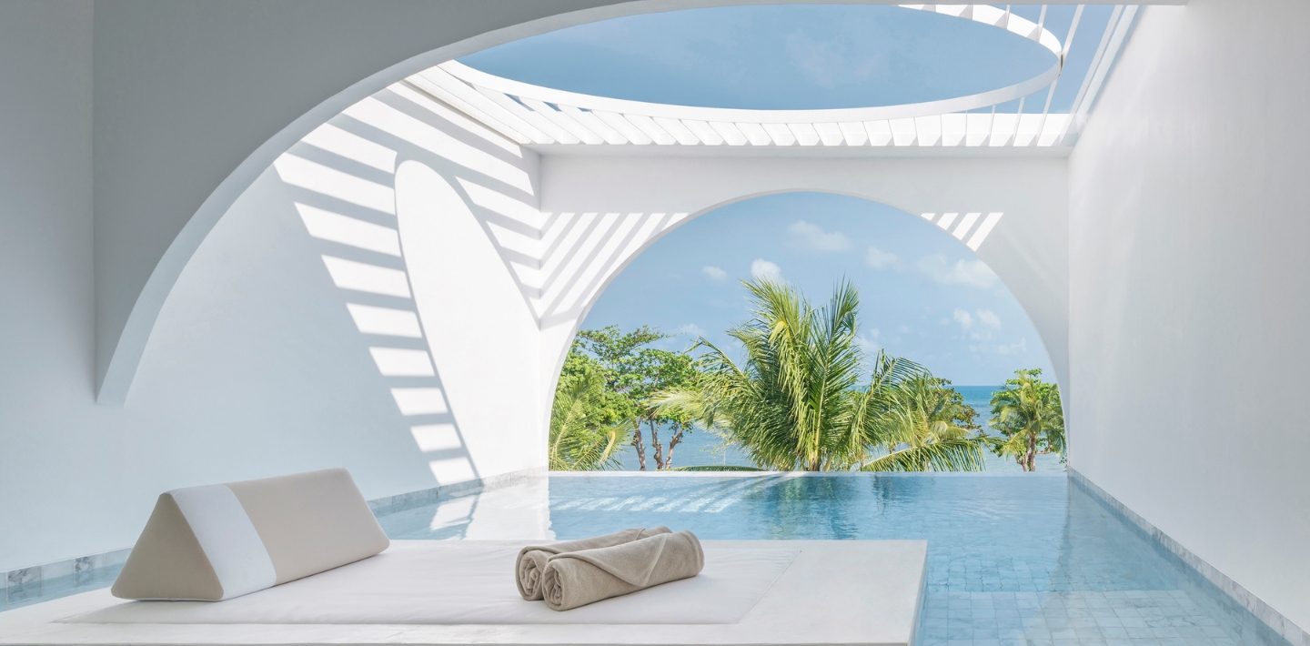 Private plunge pool and daybed under an arch looking out to palms and the sea at SALA Samui Chaweng Beach Resort