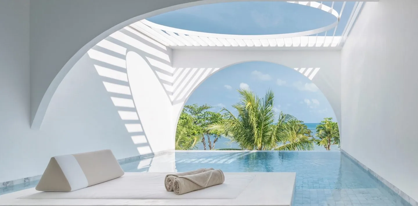 Private plunge pool and daybed under an arch looking out to palms and the sea at SALA Samui Chaweng Beach Resort
