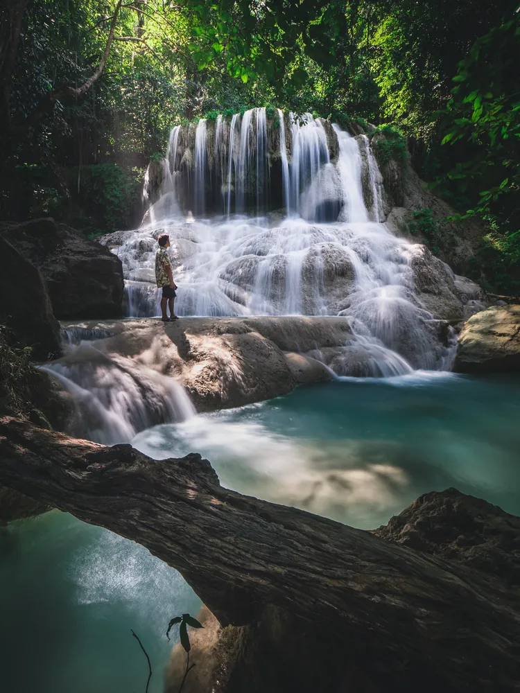 Traveller beside a tiered waterfall and turquoise pool in a forest