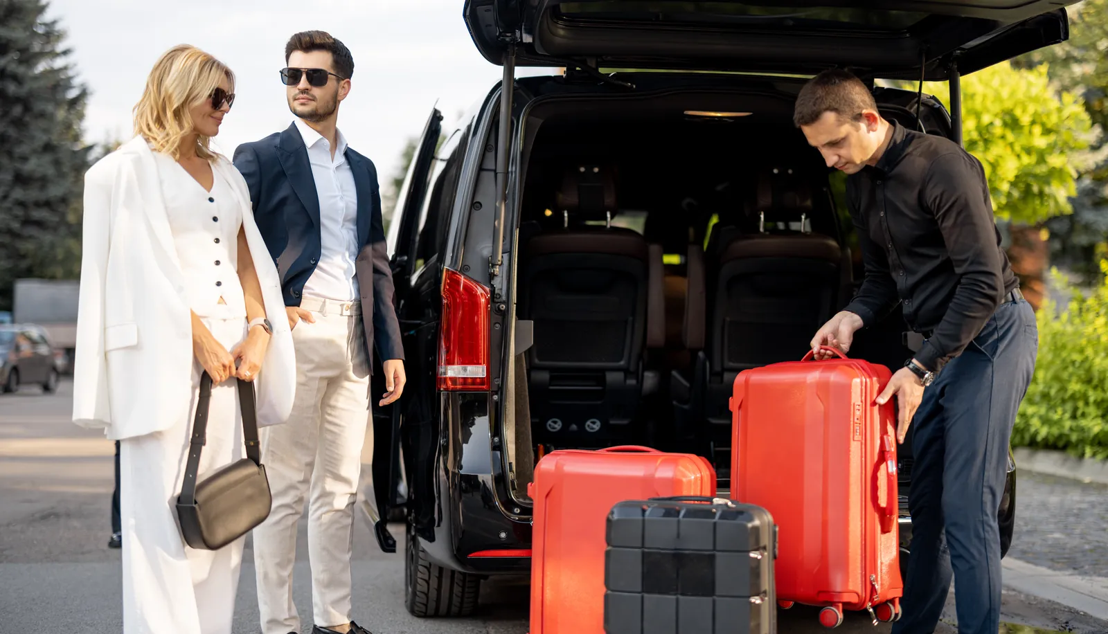 Chauffeur loading suitcases into a black passenger van for two travellers