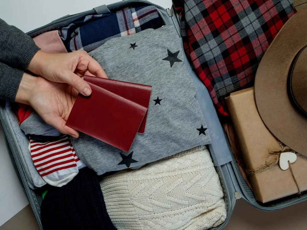 Hands holding two passports over a packed suitcase
