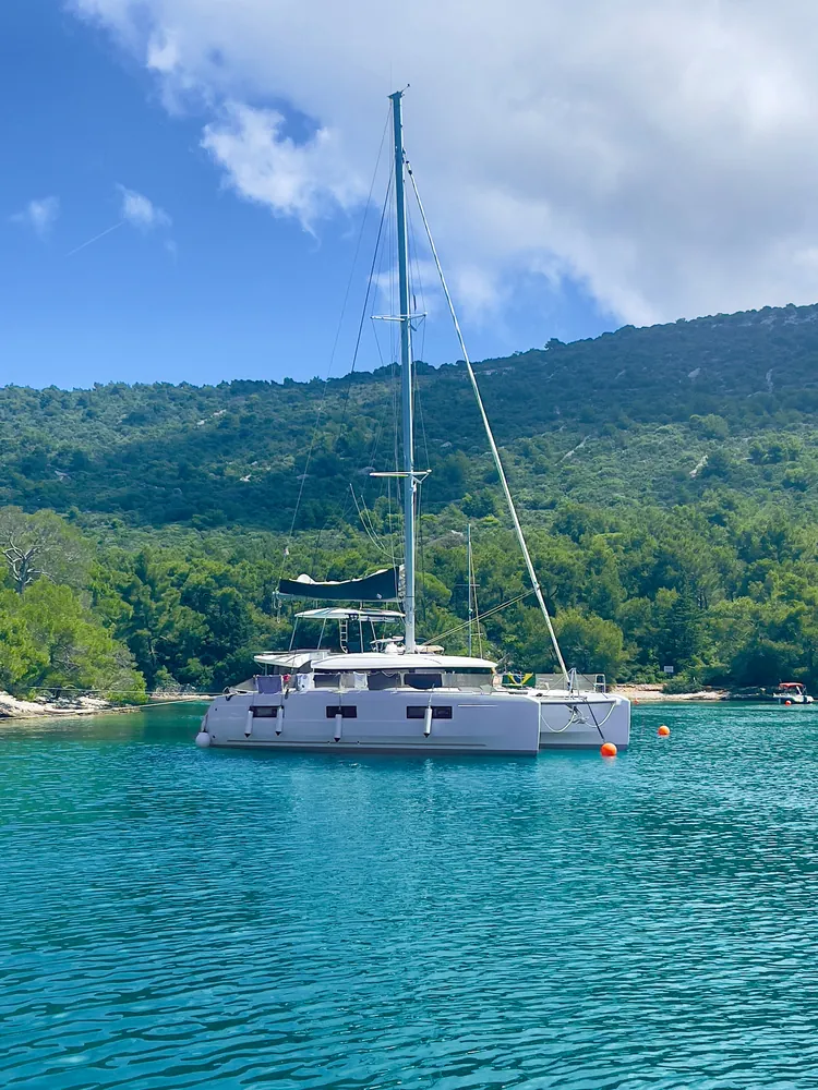 Sailing catamaran anchored in a turquoise bay below forested hills